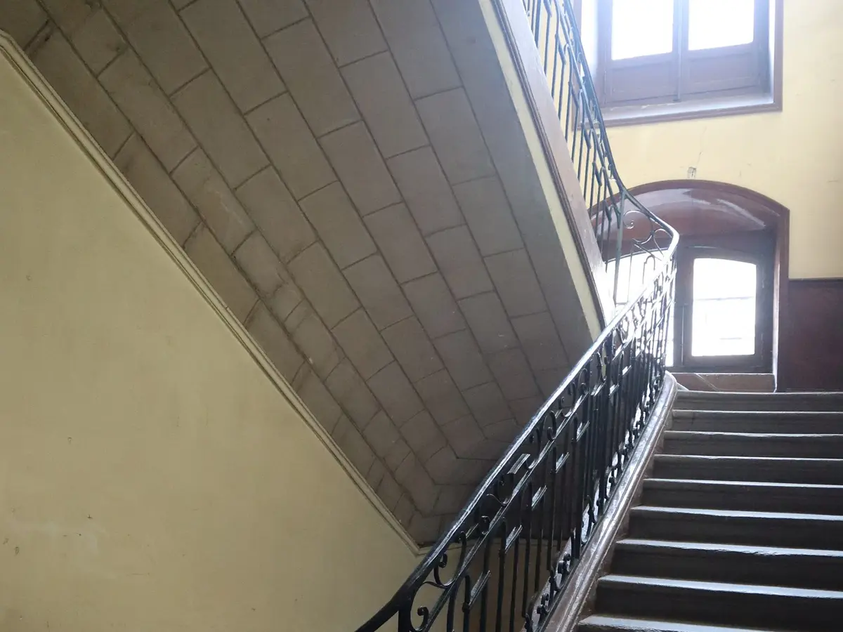 Escalier à rampe en fer forgé dans un immeuble ancien, avec ses marches et sa fenêtre
